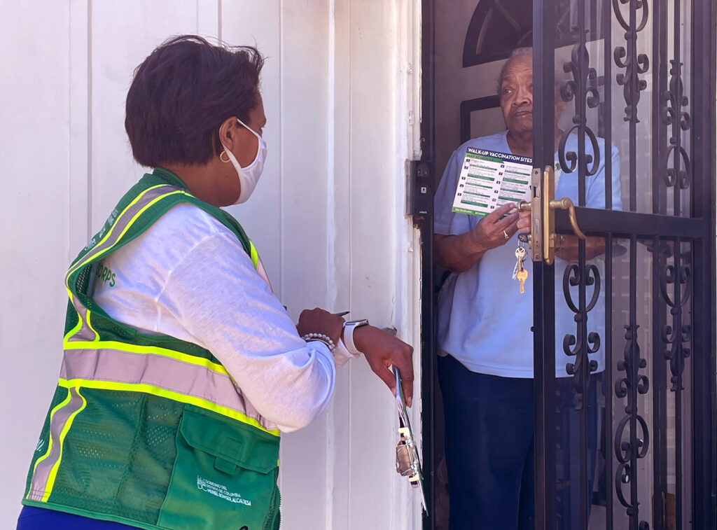 Public health worker talking, and giving printed vaccination information, to an elderly woman at her front door