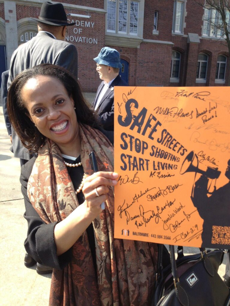 A woman at a violence prevention event in Baltimore holding a poster that reads, “Safe Streets: Stop Shooting; Start Living.”