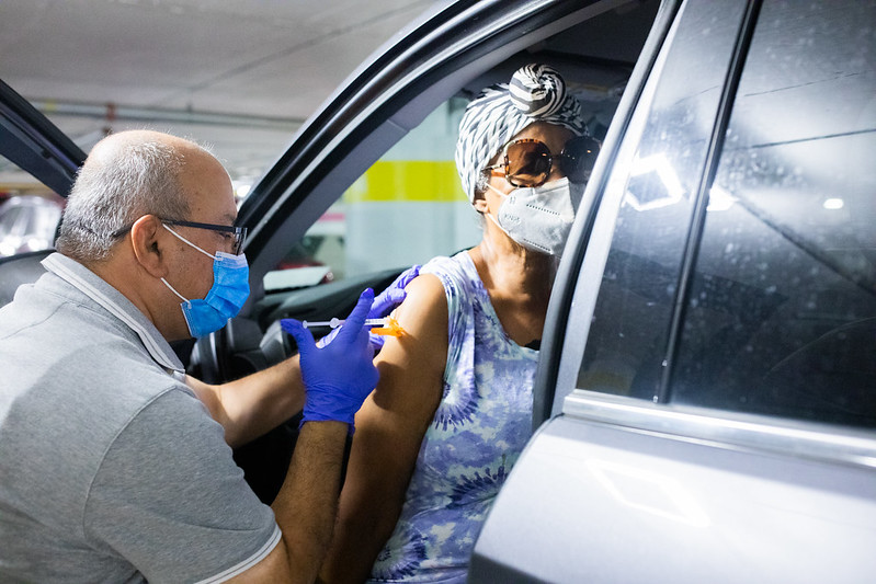 Man in Detroit wearing a face mask and giving a COVID-19 vaccine to a woman sitting in her car and wearing a face mask