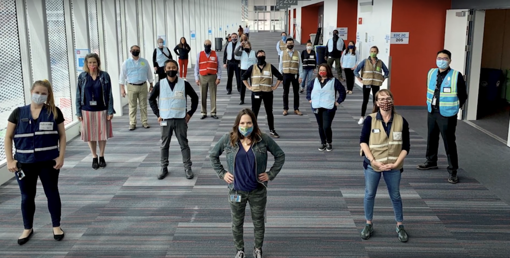 Public health workers, wearing masks, standing 6 feet apart from each other, looking confidently into the camera