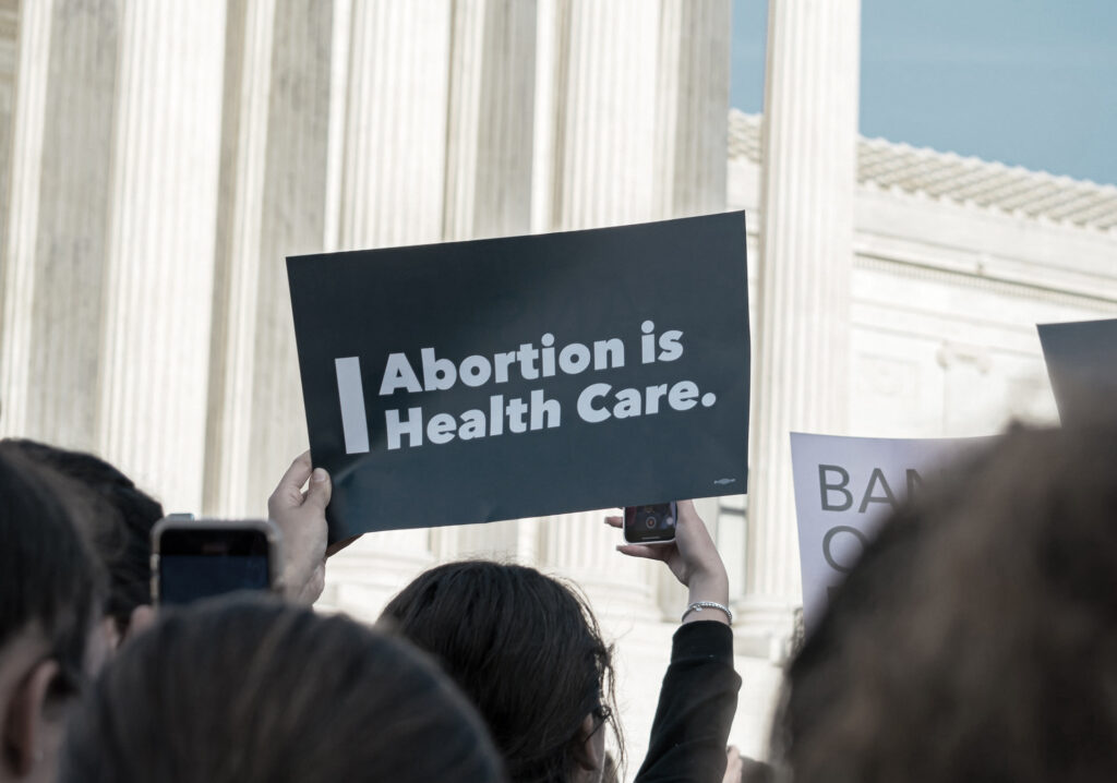 Crowd in front of Supreme Court, woman holding sign that says Abortion is Health Care. Photo by Gayatri Malhotra on Unsplash