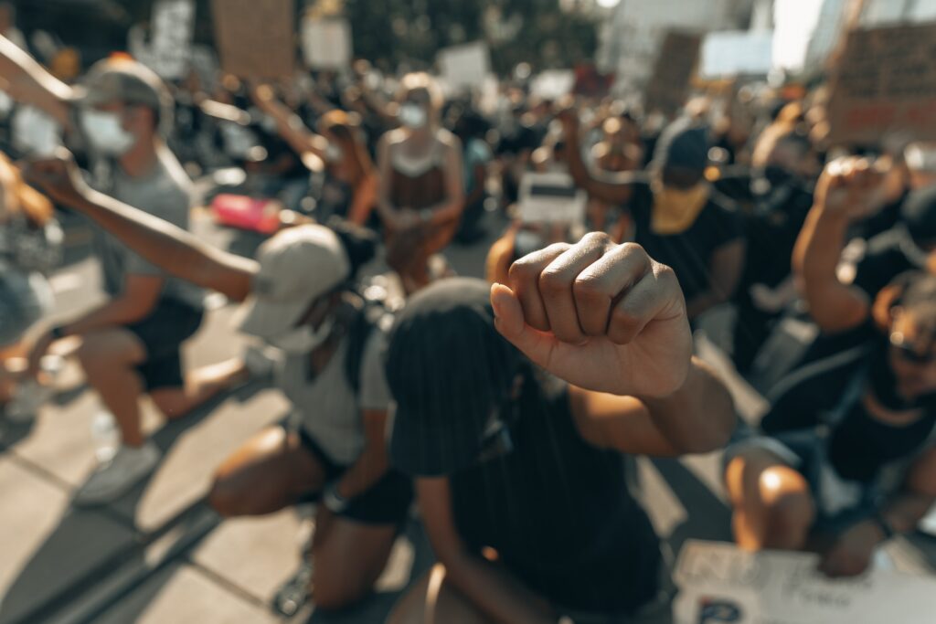 Crowd kneeling with heads bowed and fists raised. Photo by Clay Banks on Unsplash.