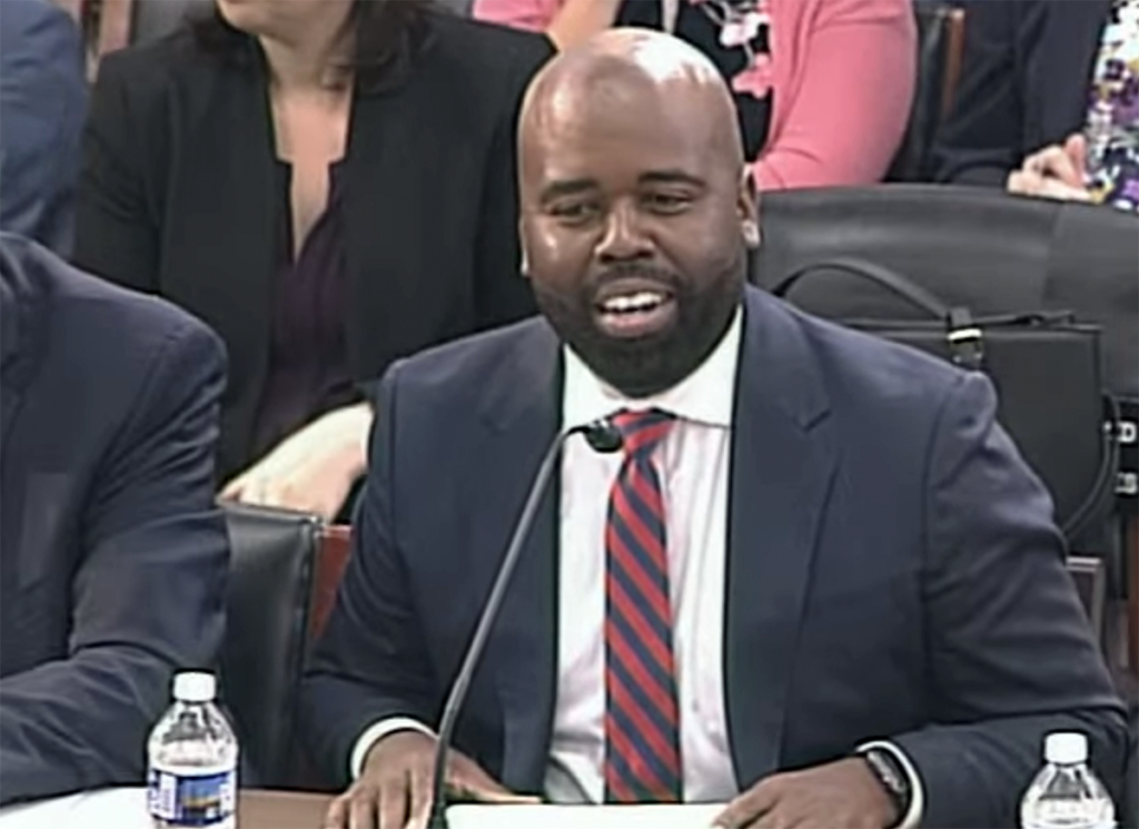 Dr. Raynard Washington sitting at a desk, speaking into a microphone, testifying before Congress