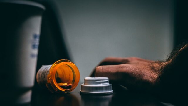 man's hand on table with open bottle of pills