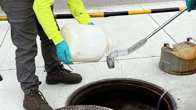 Two people collecting wastewater samples from a sewer in Boston