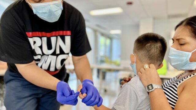 Child sitting on mother's lap gets a blood lead test from a public health worker in Baltimore