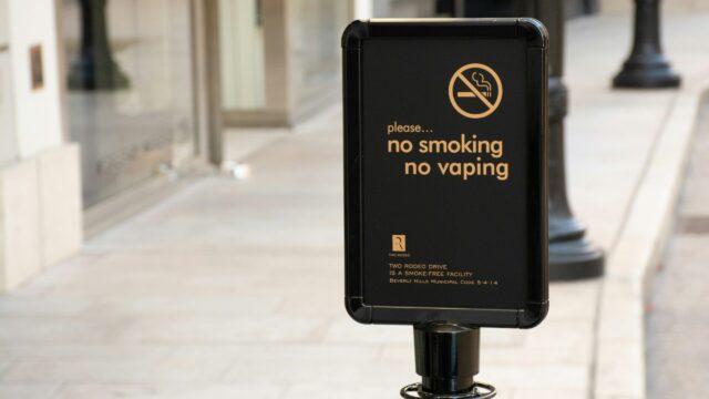 A black sign with white lettering instructing people not to smoke or vape