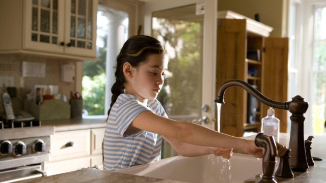 child filling glass with tap water in a kitchen