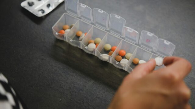 Image of a person picking up a white pill from a pill box.