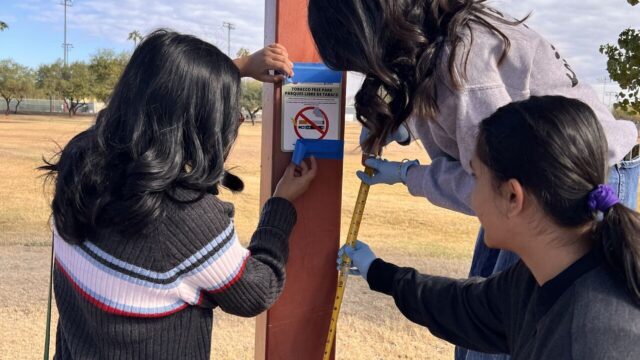 3 teens posting a no-smoking sign at a park