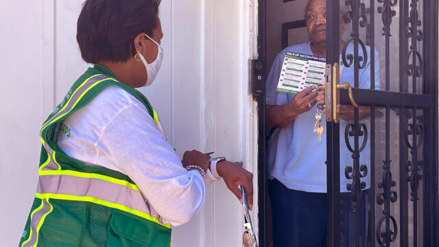 Public health worker talking, and giving printed vaccination information, to an elderly woman at her front door