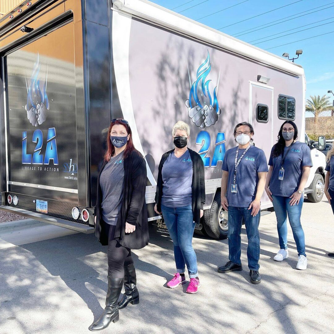 Five public health workers in masks stand in front of a mobile outreach van that reads L2A: Linkage to Action