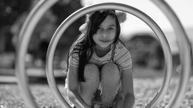 Girl peering through metal bike rack. Photo by Jairo Gonzalez on Unsplash.