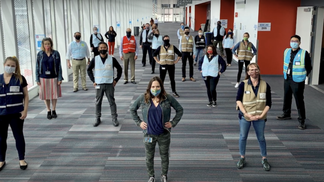 Public health workers, wearing masks, standing 6 feet apart from each other, looking confidently into the camera