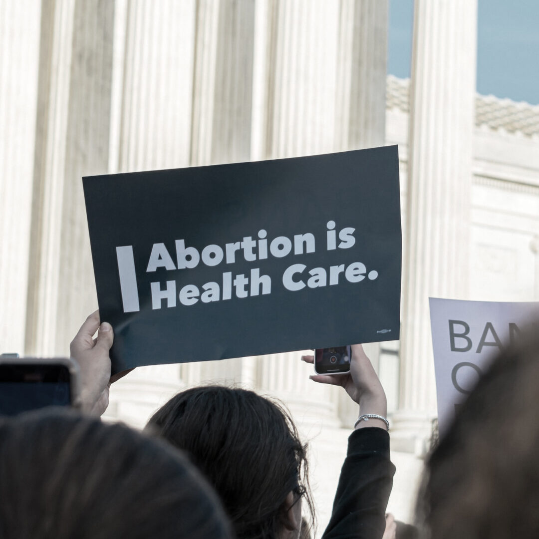 Crowd in front of Supreme Court, woman holding sign that says Abortion is Health Care. Photo by Gayatri Malhotra on Unsplash