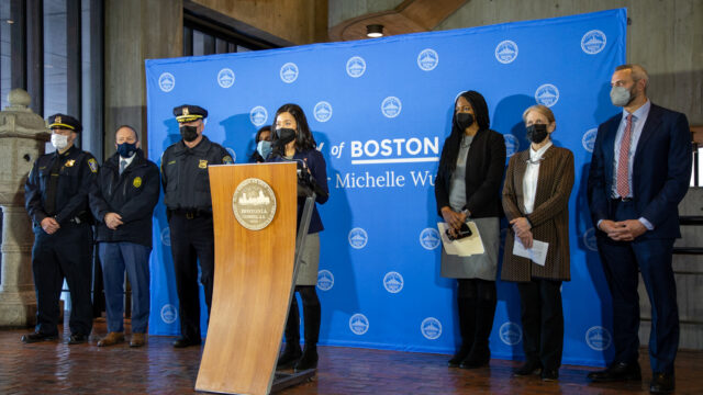 Boston Mayor Michelle Wu standing at a podium flanked by other city officials at a January 2022 briefing about the Mass and Cass housing situation