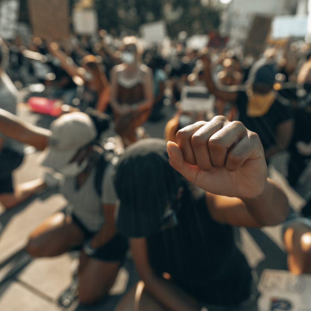 Crowd kneeling with heads bowed and fists raised. Photo by Clay Banks on Unsplash.