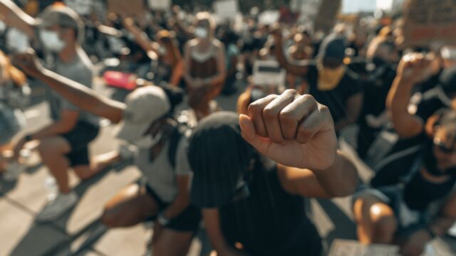 Crowd kneeling with heads bowed and fists raised. Photo by Clay Banks on Unsplash.