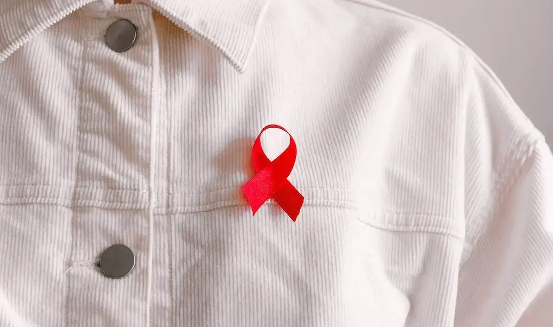 Person in white button up shirt with a red ribbon on their chest. Photo by Anna Shvets.