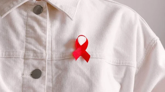 Person in white button up shirt with a red ribbon on their chest. Photo by Anna Shvets.