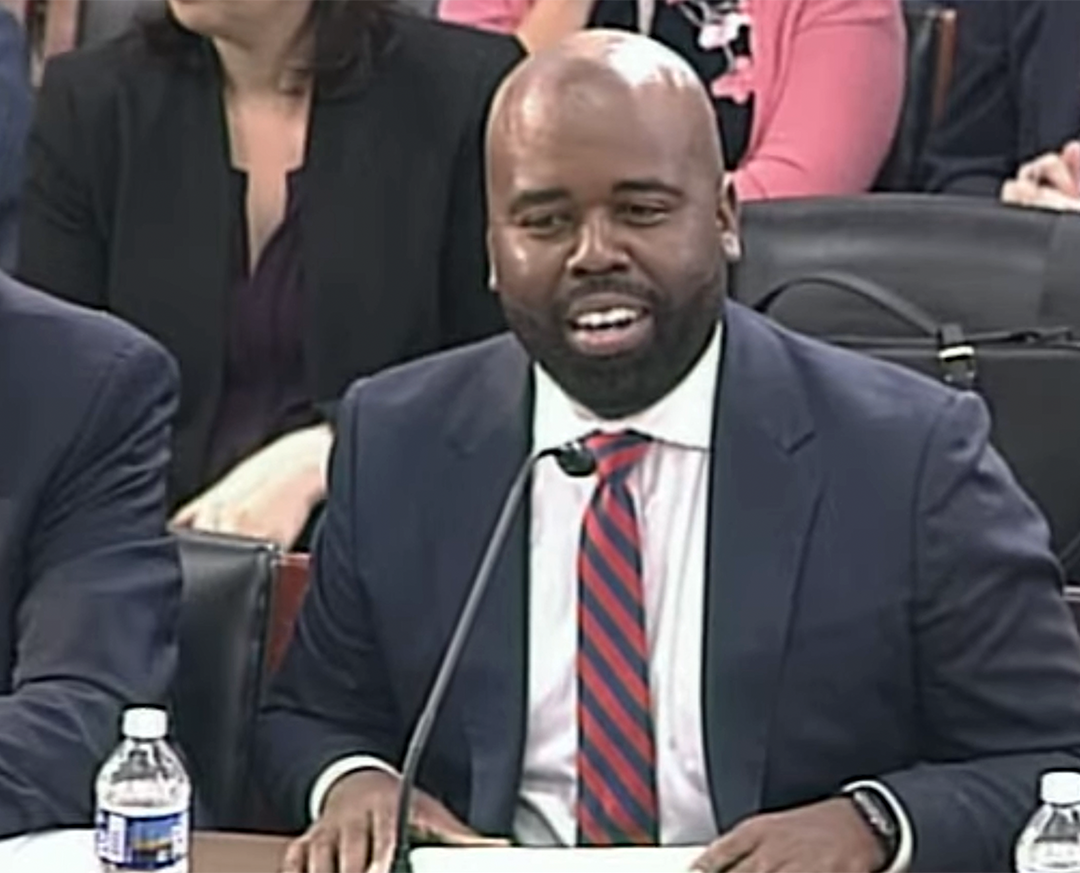 Dr. Raynard Washington sitting at a desk, speaking into a microphone, testifying before Congress