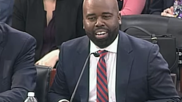 Dr. Raynard Washington sitting at a desk, speaking into a microphone, testifying before Congress