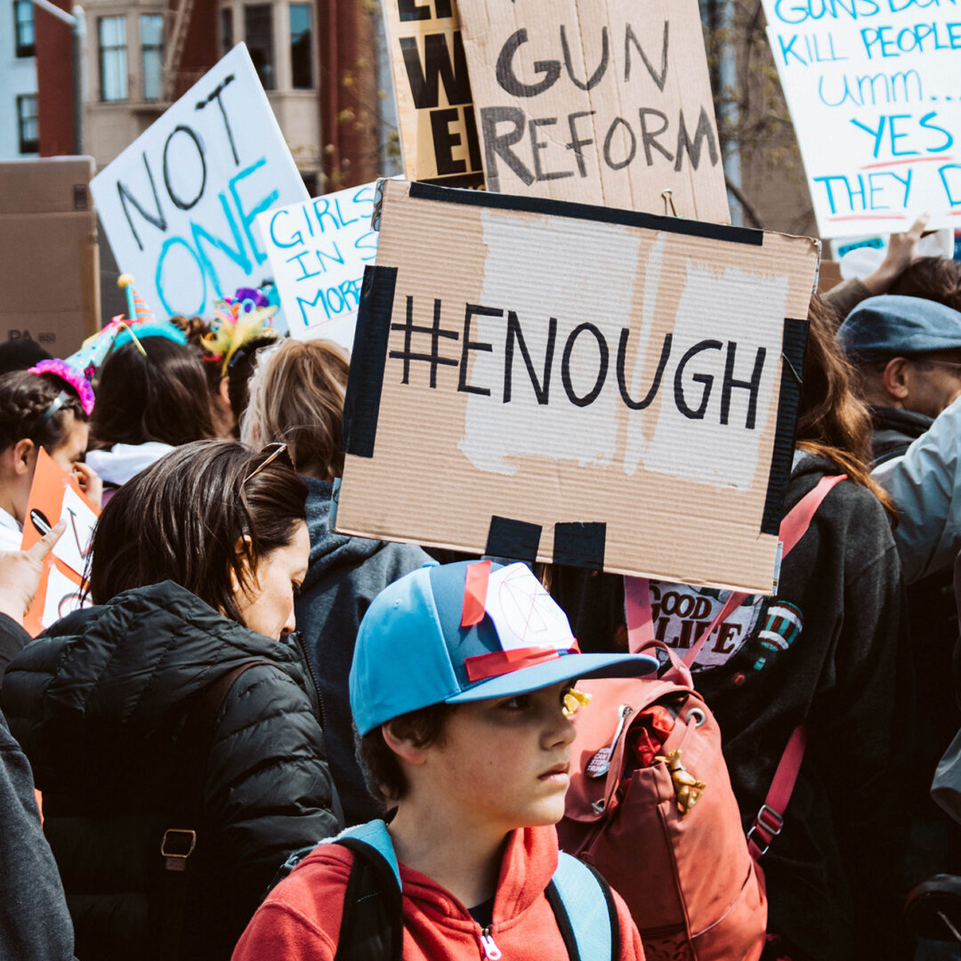 Anti-gun violence protest with child standing in foreground. Photo by Natalie Chaney on Unsplash.